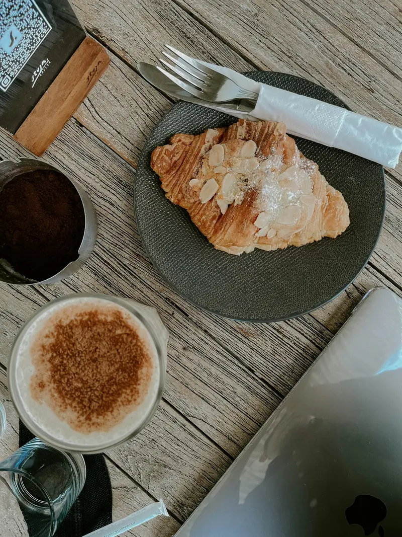 Coffee and an almond croissant on a wooden table.